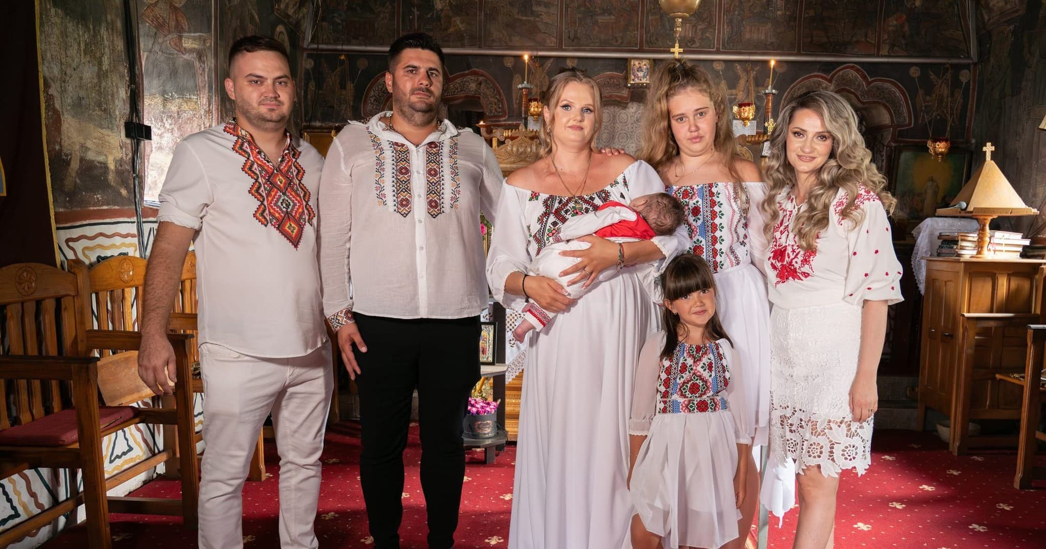 Familie în ii tradiționale la botez, în biserică, cu bebelușul în brațele mamei